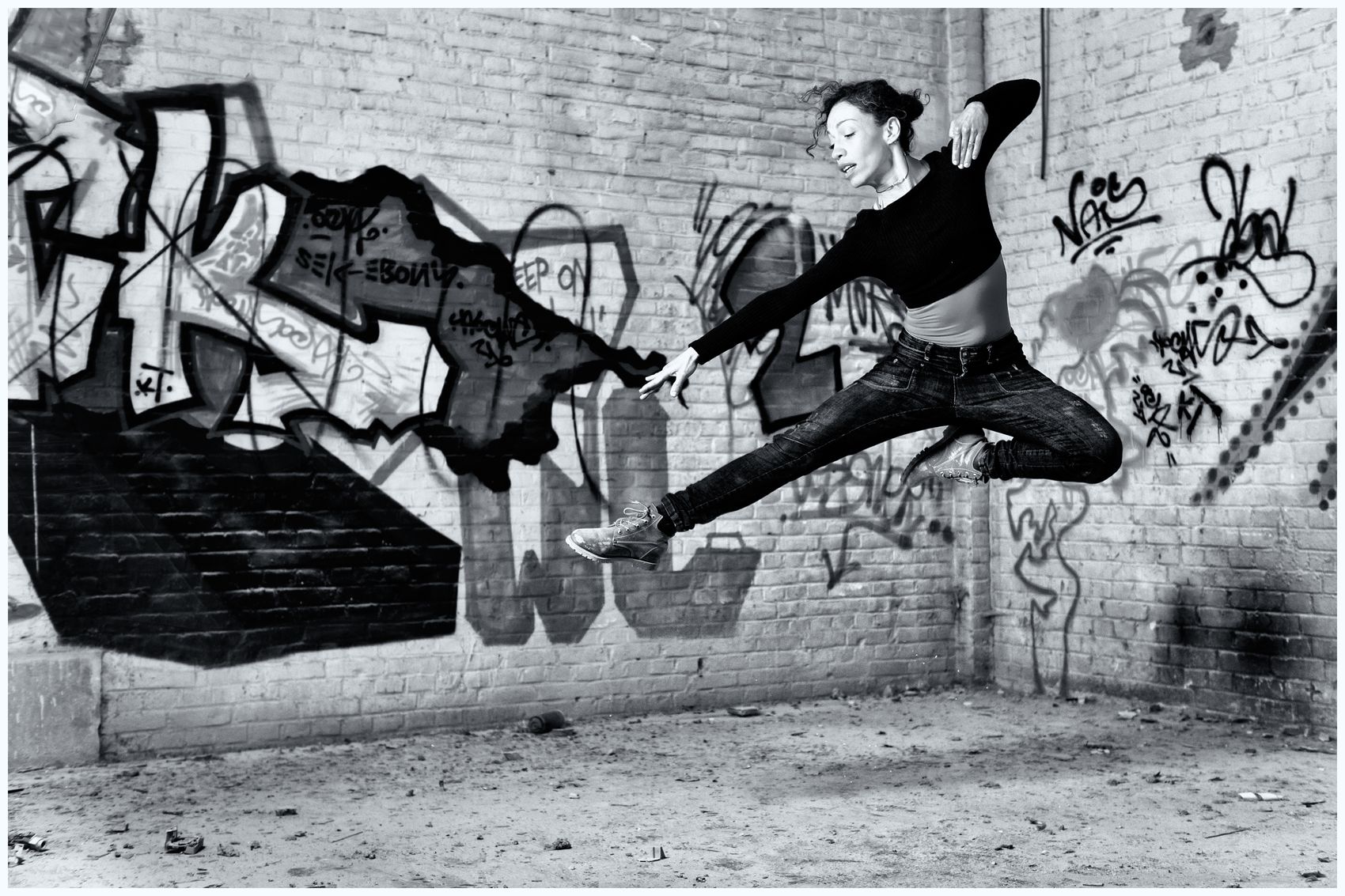 Danseres springt voor een graffitimuur, zwart-wit